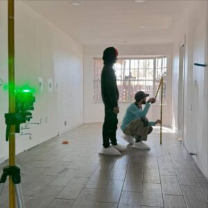 General contractors using a laser level and measuring tape in a room with new flooring during a remodel by Forged Builds Custom Remodels in El Paso, TX.