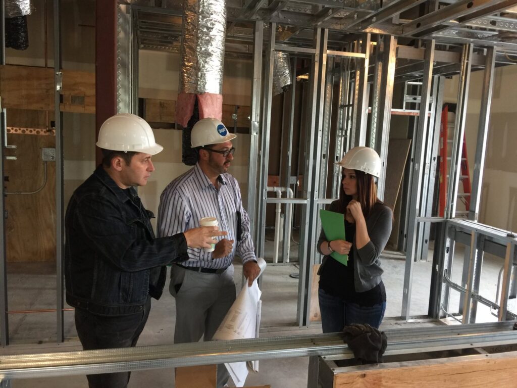 General contractors and clients reviewing blueprints on a commercial construction site with exposed framing and ductwork by Siegel Construction in Eugene, OR.