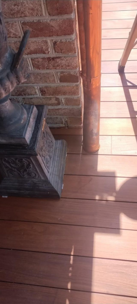 A newly installed copper downspout next to a brick wall and wooden deck by Charleston Exteriors in Charleston, SC.