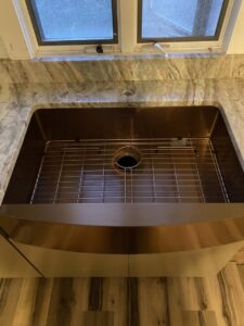A large, single-basin copper-toned farmhouse sink expertly installed into a granite countertop by Fine Design Marble And Granite in Springfield, MA.
