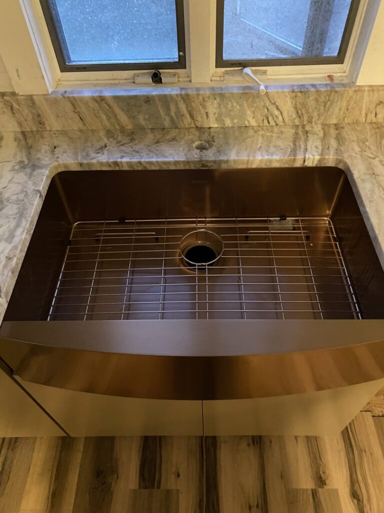 A large, single-basin copper-toned farmhouse sink expertly installed into a granite countertop by Fine Design Marble And Granite in Springfield, MA.