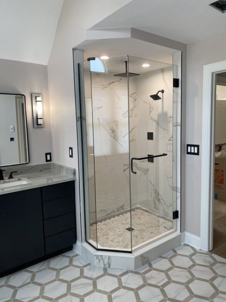 A newly installed corner glass shower enclosure with a pebble floor and marble-look tiles by CLE Remodeling Co in Cleveland, OH.