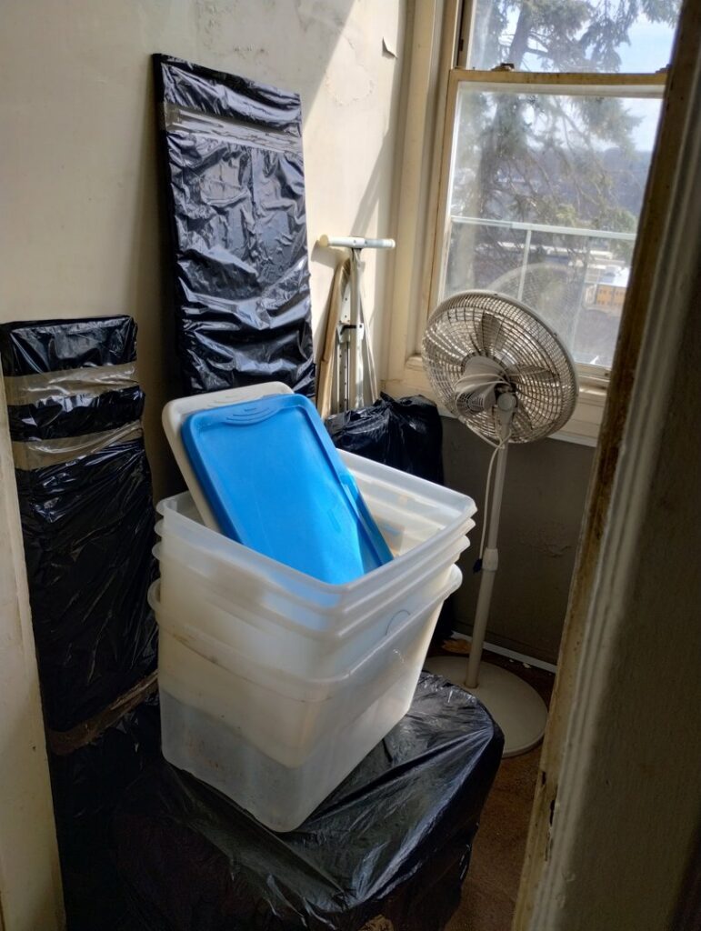 A corner of a room with plastic bins, black trash bags, and a fan, indicating items ready for junk removal by Ron's Rubbish & Junk Removal Cleanout Services in Yonkers, NY.