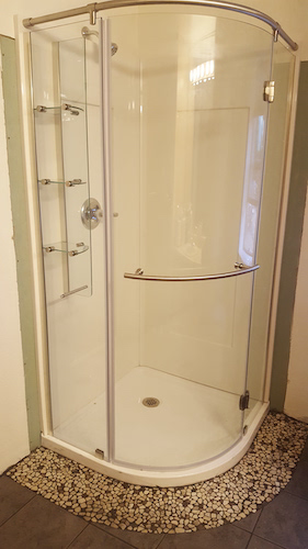 Corner shower unit installation with pebble flooring by Girard Builders in Medford, OR.