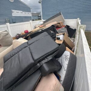Couch cushions, a mattress, and boxes piled inside a fenced area for junk removal by Veterans Easy Trash: Atlanta in Atlanta, GA.