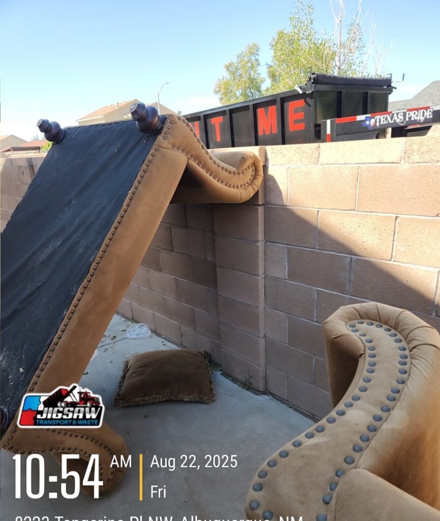 A couch ready for removal, with a dump trailer from Jigsaw Transport and Waste visible in the background in Albuquerque, NM.