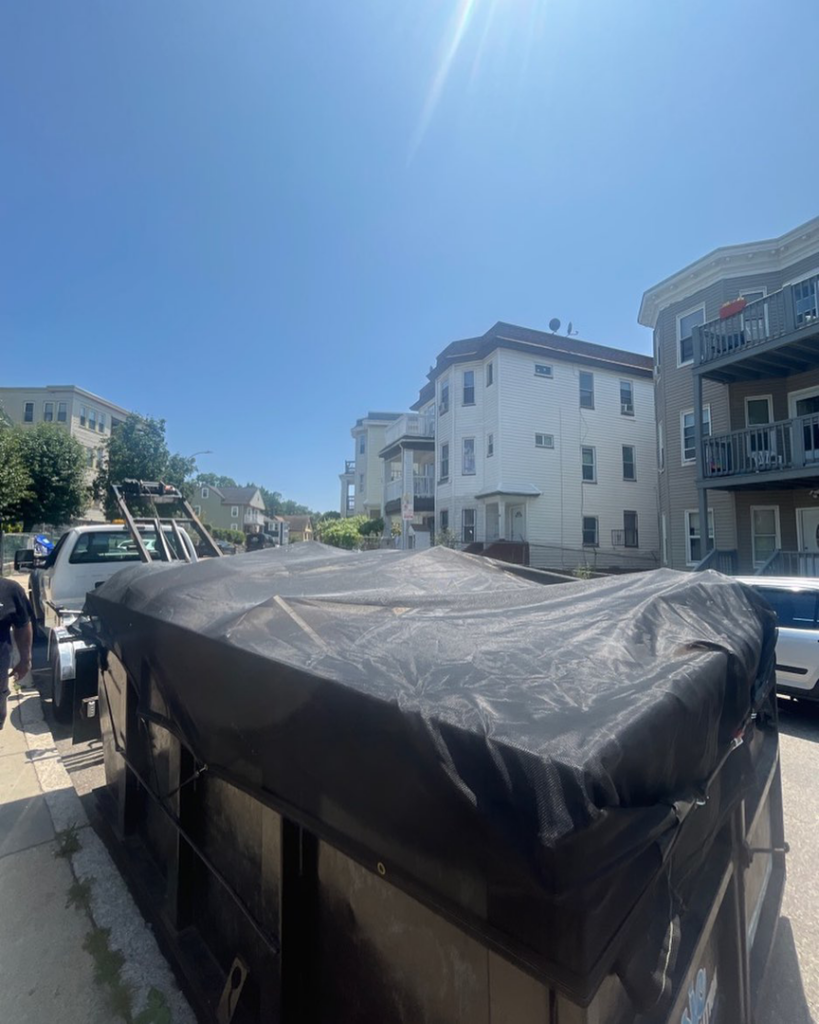 A covered Classic Disposal dumpster on a truck, parked on a residential street in Malden, MA, ready for transport.