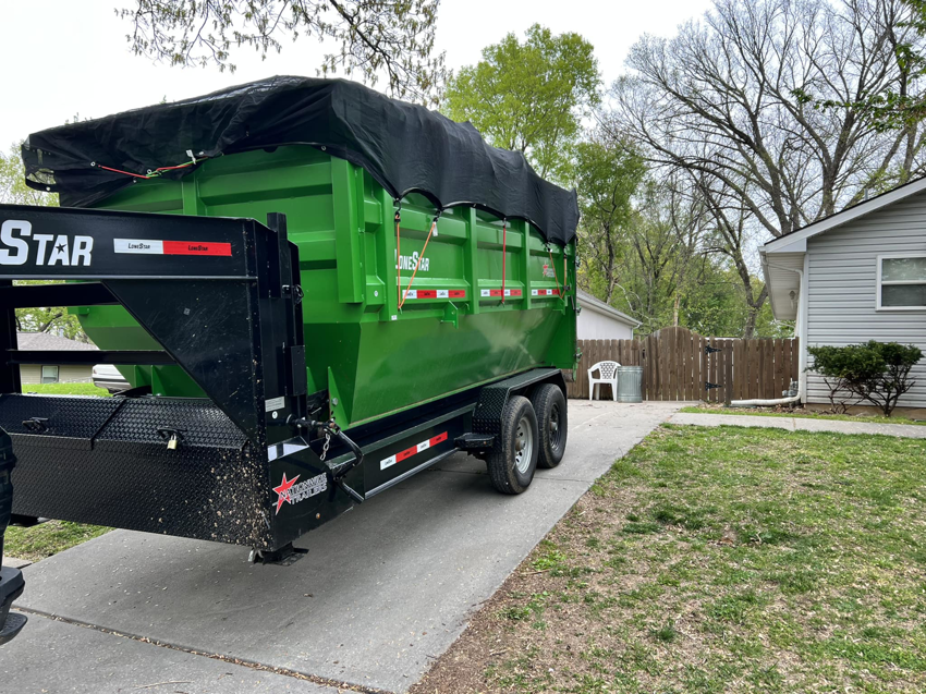 A covered green dumpster trailer parked in a residential driveway, ready for pickup or delivery by Proper Dumpster Rentals in Kansas City, KS.