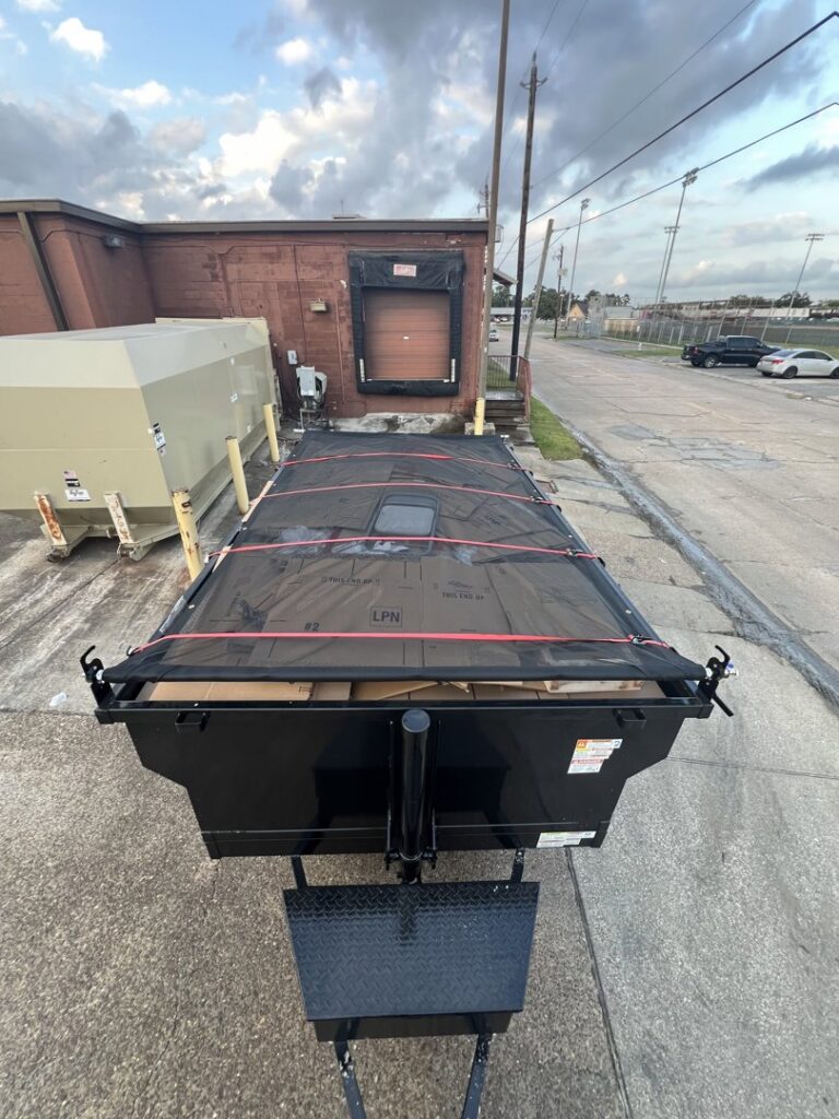 A dump trailer, covered and secured, filled with junk outside a commercial building, ready for hauling by Tidy Loaders Junk Removal in Houston, TX.