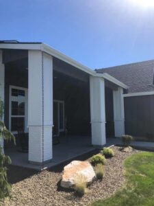 A newly constructed covered patio with white columns and rain chains on a house exterior by The Huckleberry Handyman in Meridian, ID.