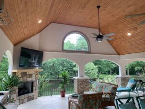 A comfortable covered patio featuring a stone fireplace, mounted TV, and ample seating by Technically Aesthetic General Contractors in Johnson City, TN.
