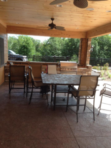 A comfortable covered patio with outdoor dining furniture and a built-in grill, designed by Ankeny Builders L.L.C. in Eau Claire, WI.
