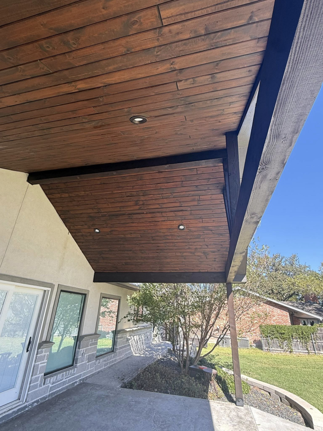 A covered outdoor patio featuring a dark wood plank ceiling and recessed lighting, attached to a house exterior by Javier's Painting in San Angelo, TX.