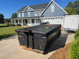 A black roll-off dumpster with a protective tarp from Jr's Mini Roll Off LLC in a residential driveway in Byron, GA.