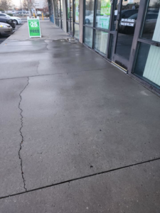 A cracked concrete sidewalk in front of a commercial building, a common repair job for Duran Landscaping in Albuquerque, NM.
