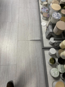 Cracked floor tiles with a visible gap near a retail display, showing a floor repair project by Byrd Property Restoration, LLC in Parkersburg, WV.