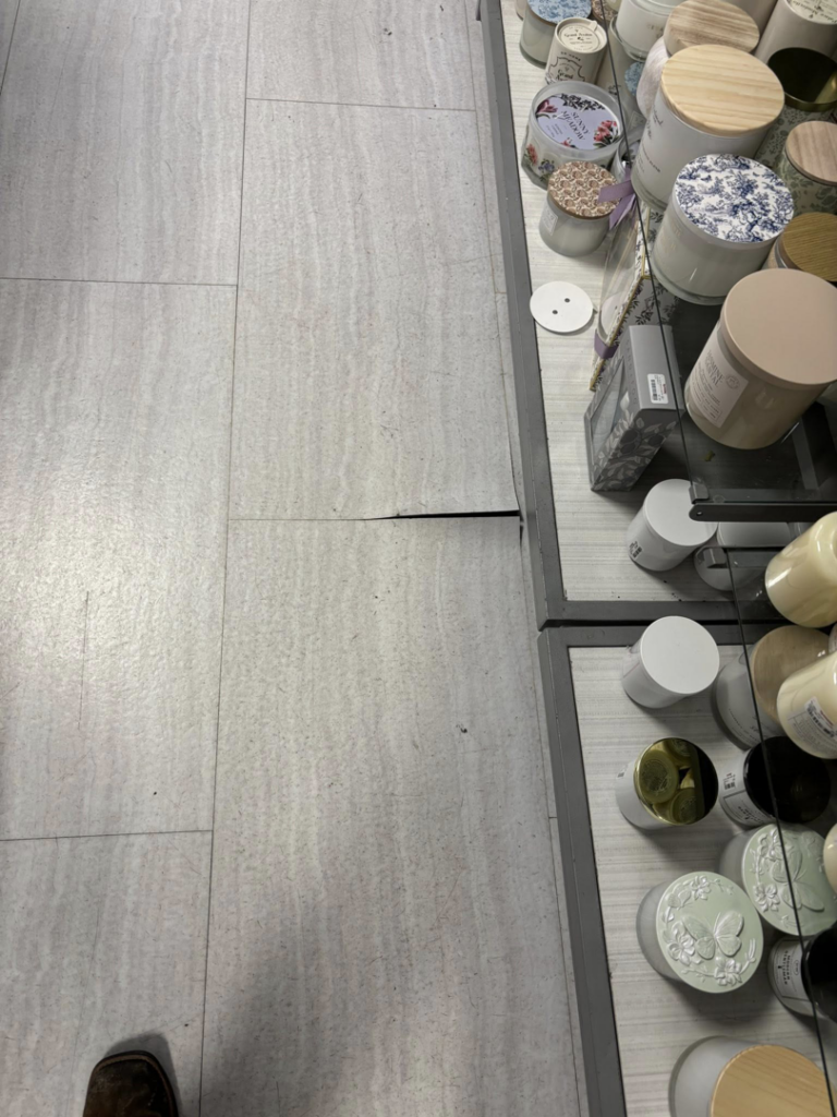 Cracked floor tiles with a visible gap near a retail display, showing a floor repair project by Byrd Property Restoration, LLC in Parkersburg, WV.