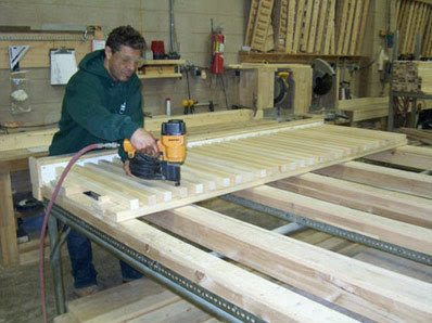 A craftsman assembling a wood fence panel with a nail gun at Fence Factory Inc's workshop in Stamford, CT