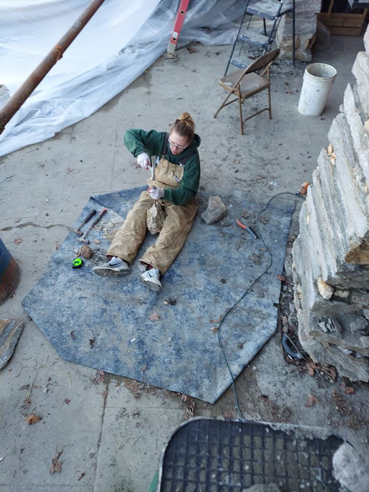 A craftsperson in overalls shaping a stone for masonry restoration at Stone cutter masonry restoration & waterproofing in Georgetown, KY.