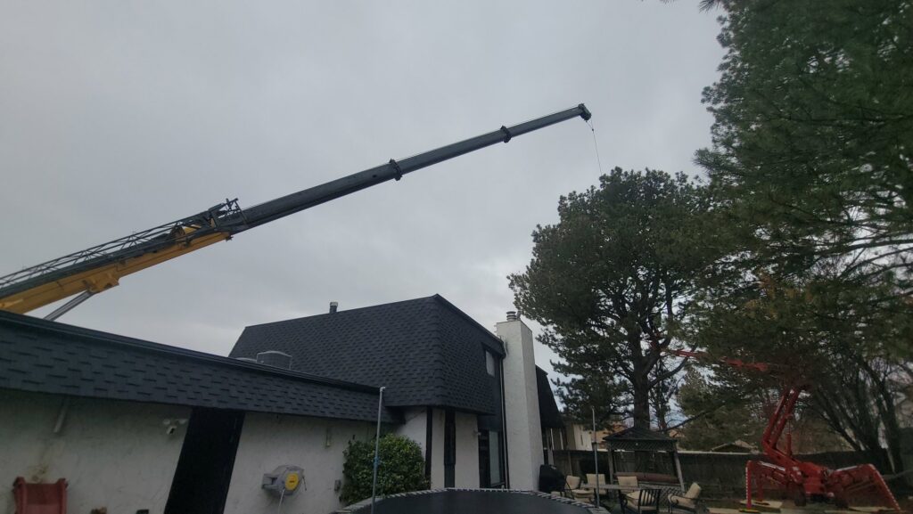 A crane and a red spider lift, heavy equipment used by My Tree Guys, LLC for tree service, extending over a house in Salt Lake City, UT.