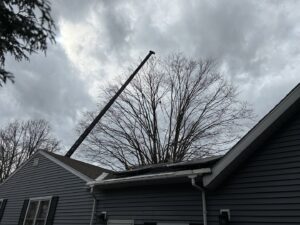 A crane boom extends over a house, indicating tree removal or heavy pruning by Savatree Burlington, VT.