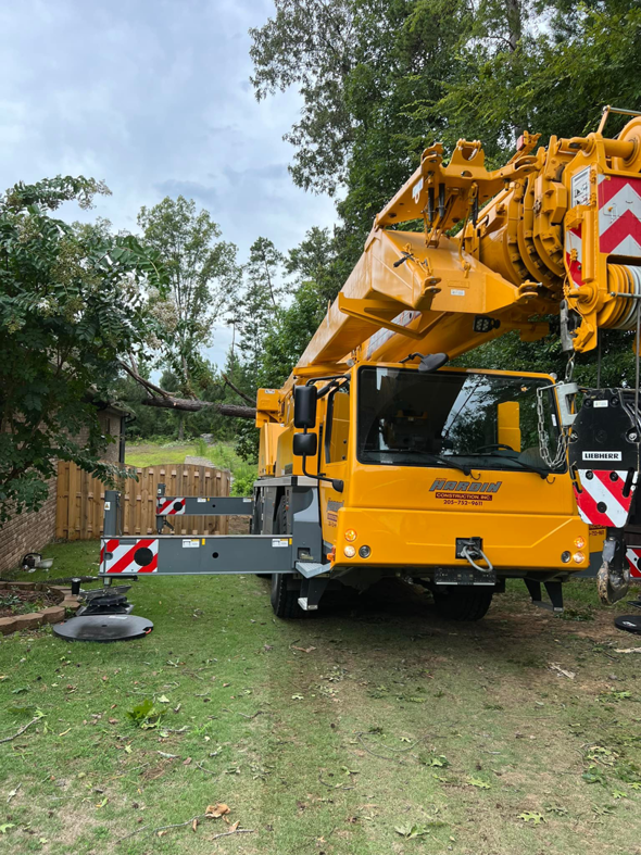 A large yellow crane is positioned on a lawn, ready for heavy tree removal work by Ellison's Tree Service in Northport, AL.