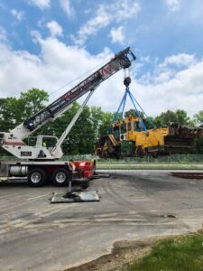 A crane from Tidewater Crane & Contracting lifting heavy yellow machinery at an outdoor site in Virginia Beach, VA