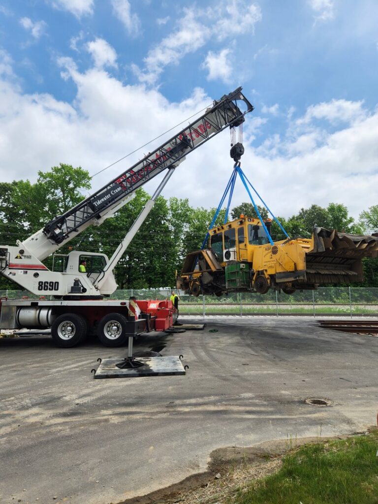 A crane from Tidewater Crane & Contracting lifting heavy yellow machinery at an outdoor site in Virginia Beach, VA