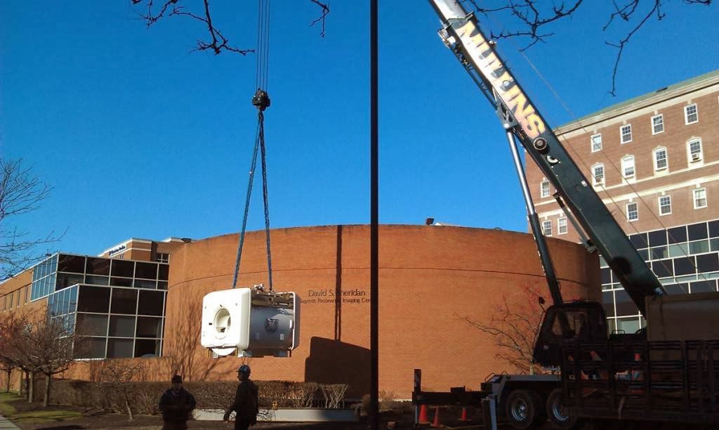A Mullins Rigging crane lifting specialized medical equipment outside a building in Green Island, NY