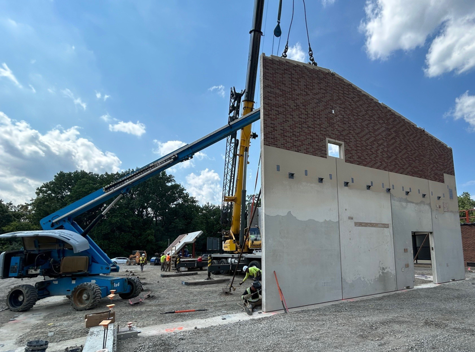 A large crane lifting a precast concrete panel with a brick facade at a construction site by Lombard Architectural Precast Products Company in Aurora, IL.