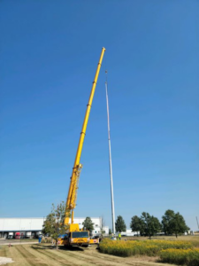 A large yellow crane lifting a tall pole at a job site by Midwest Crane & Rigging Inc. in Belvidere, IL