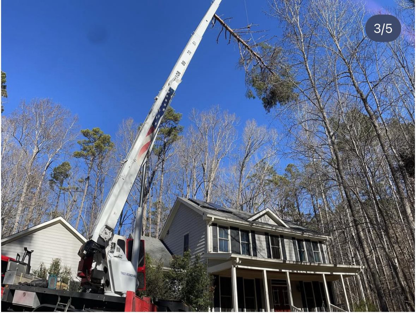 A crane carefully lifting a large tree branch over a residential house during tree removal by MacNeela's Tree Service in Durham, NC