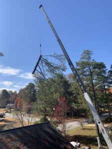 A crane lifting a tree branch over a residential roof during tree service by 706 Tree and Stump in Augusta, GA.