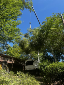 A crane carefully lifting a large tree branch over a residential property by Timber Tree Service Incorporated in Theodore, AL.