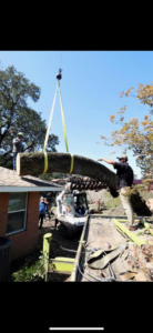 Tree service crew using a crane to lift a large tree trunk over a house during removal by Green Leaf Tree Service in Broussard, LA.