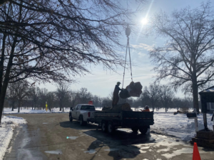 A crane lifting a large tree trunk section onto a trailer during a tree removal job for S.M.B Family Tree Service in House Springs, MO.