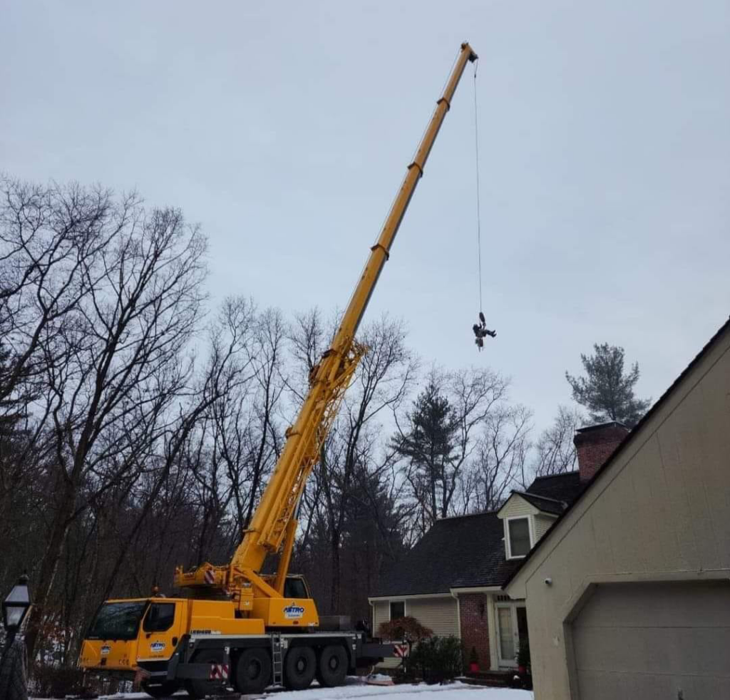 A large crane lifting a worker or equipment for safe tree removal by Out On A Limb Tree Service in Lowell, MA.
