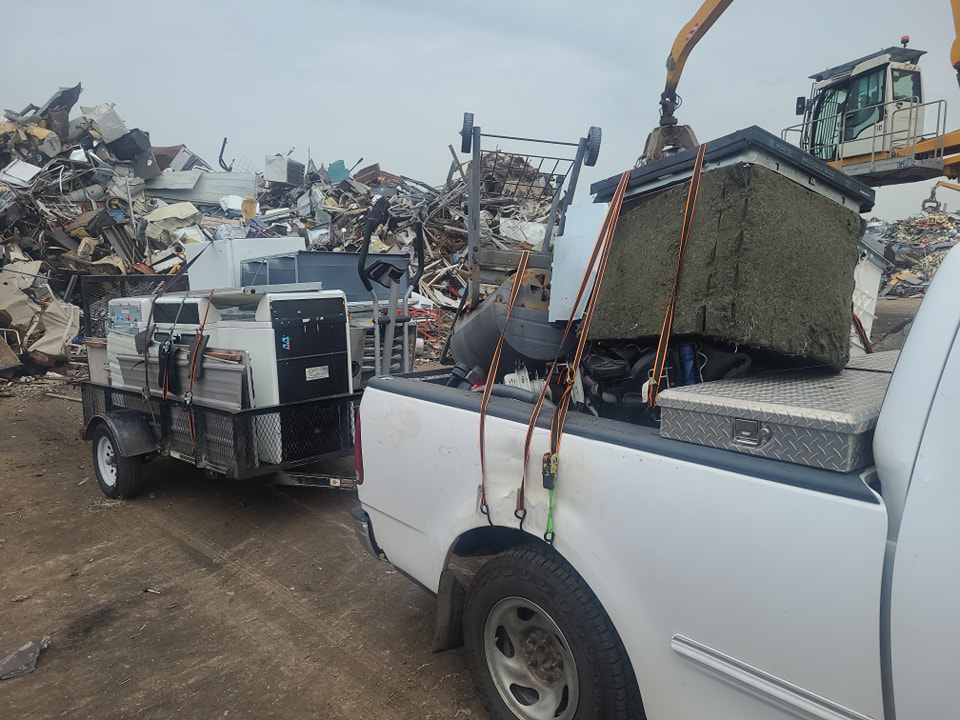 A crane loading scrap metal onto a pickup truck and trailer at GJR Scrap Metals in Kansas City, MO.