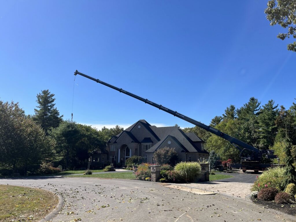 A large crane with its boom extended over a residential house, set up for a tree removal project by Tip Top Tree Service in Hudson, NH.