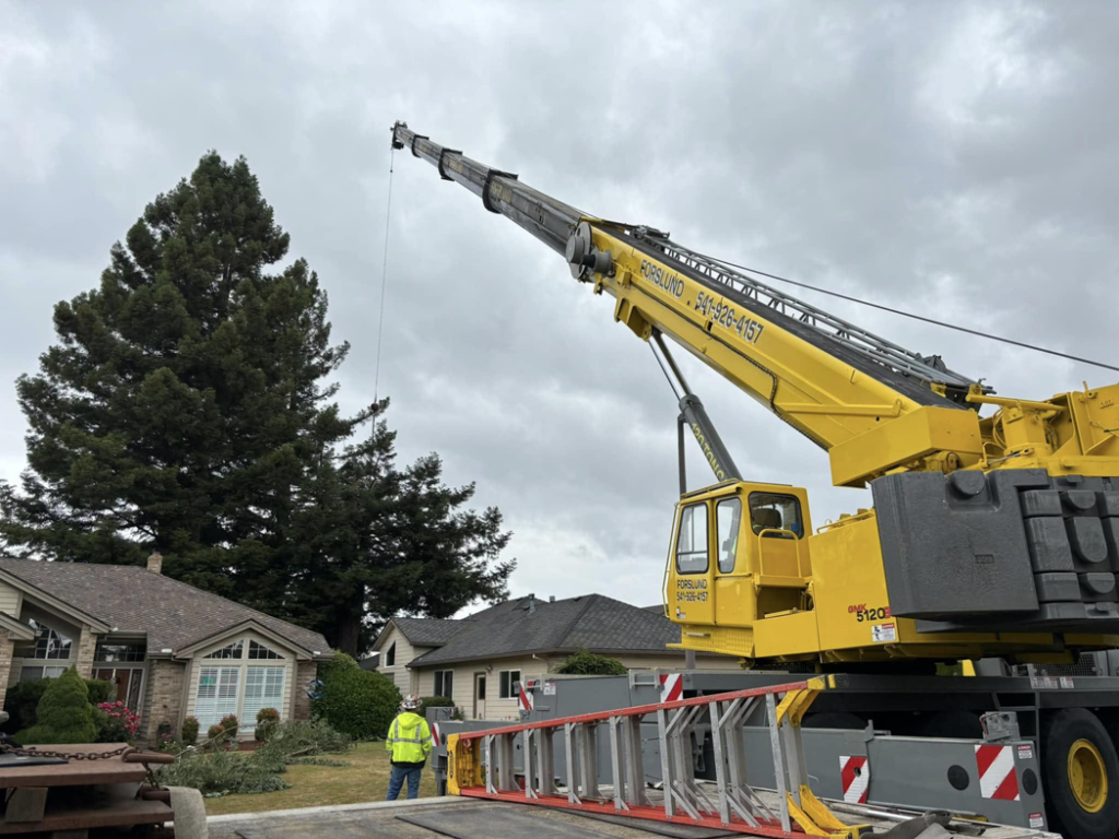 A large crane set up for tree removal or trimming, with a worker nearby, by Caudle's Tree Service in Salem, OR