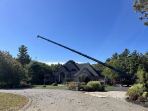 A large crane set up for tree removal operations over a residential property by Tip Top Tree Service in Hudson, NH.