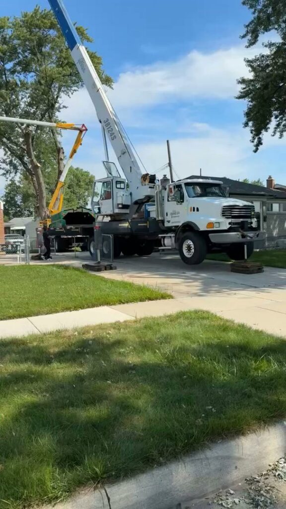 A large crane truck and a bucket lift truck are set up on a driveway for a tree service job by Magee Tree Service in Detroit, MI.