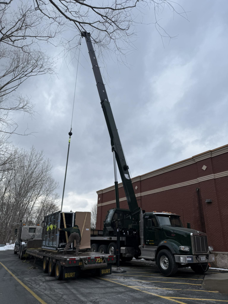 A BURT crane & rigging truck lifts crated equipment from a flatbed trailer at a construction site in Green Island, NY.