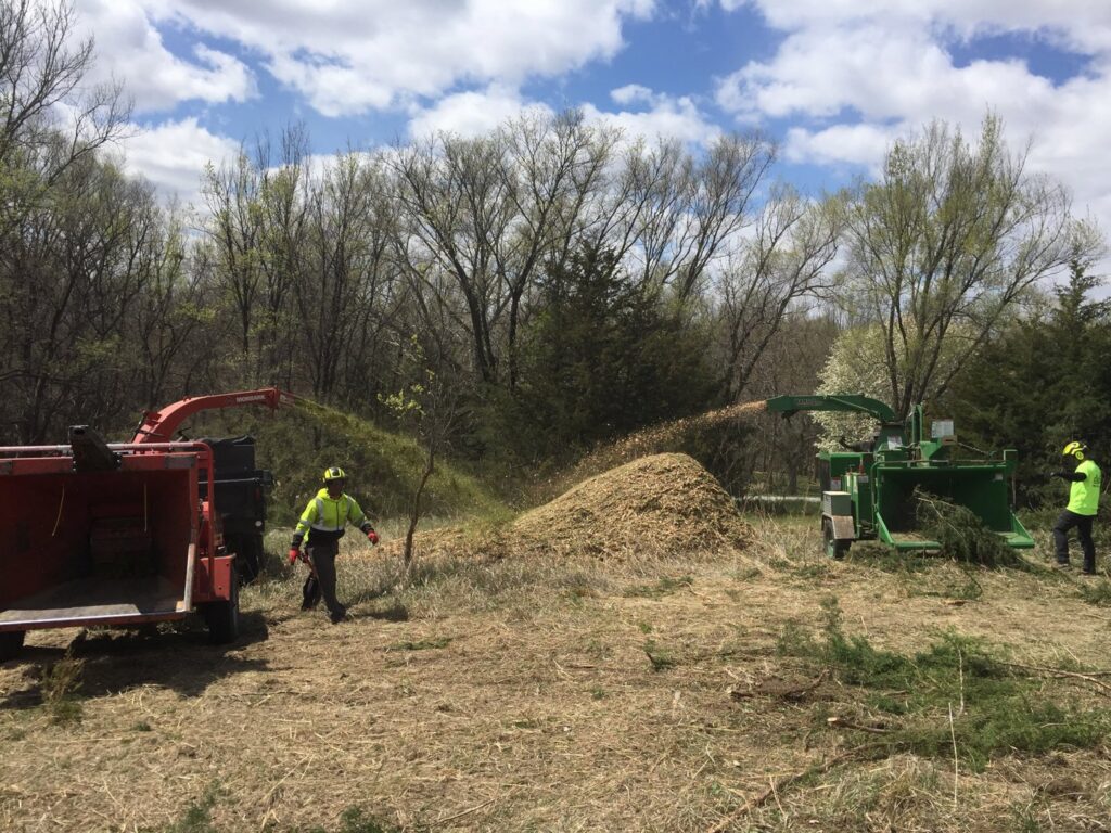 A large crane truck from Monster Tree Service of Omaha, NE, is set up on a residential driveway for a tree removal or trimming job.