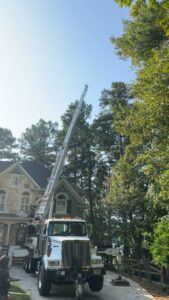 A crane truck with its boom extended over a residential house for tree trimming by Trinity Tree Service in Cumming, GA.