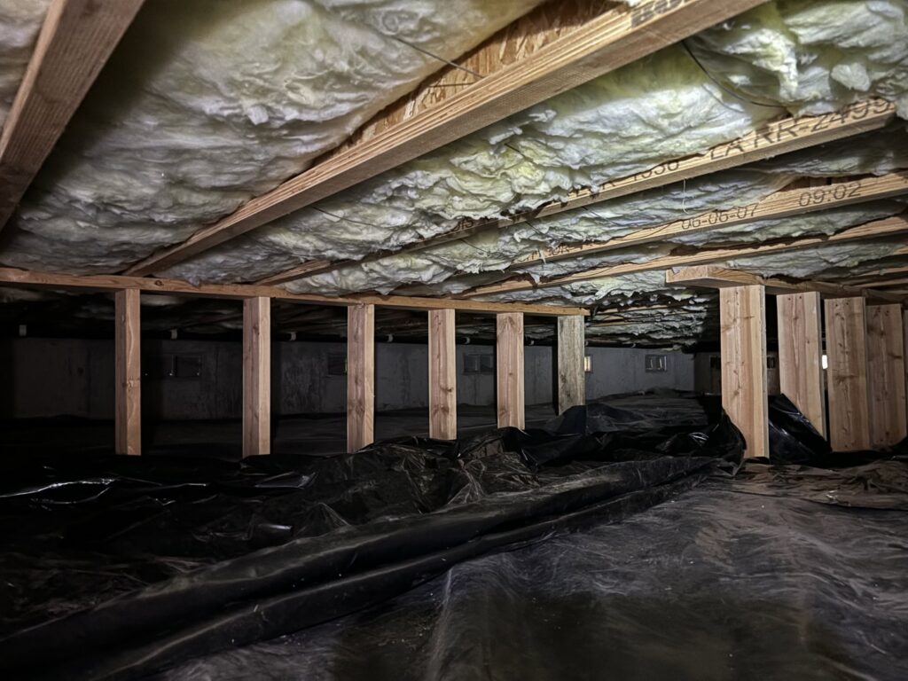 Crawl space with insulation between floor joists and a new vapor barrier installed by Pacific Insulation & Mold Remediation in Spokane, WA.