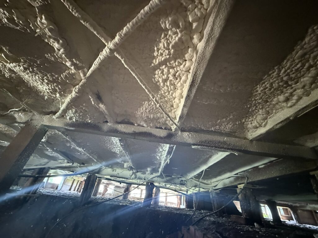 Crawl space with spray foam insulation on joists and pipes by IFOAM Insulation of Hill Country, a general contractor in San Antonio, TX