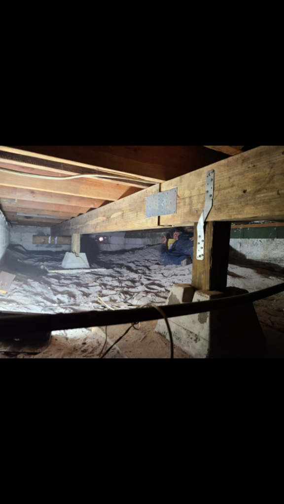 A worker performing structural repair in a crawl space with wooden beams and concrete supports by Snapp Industries, Inc. in Miami, FL