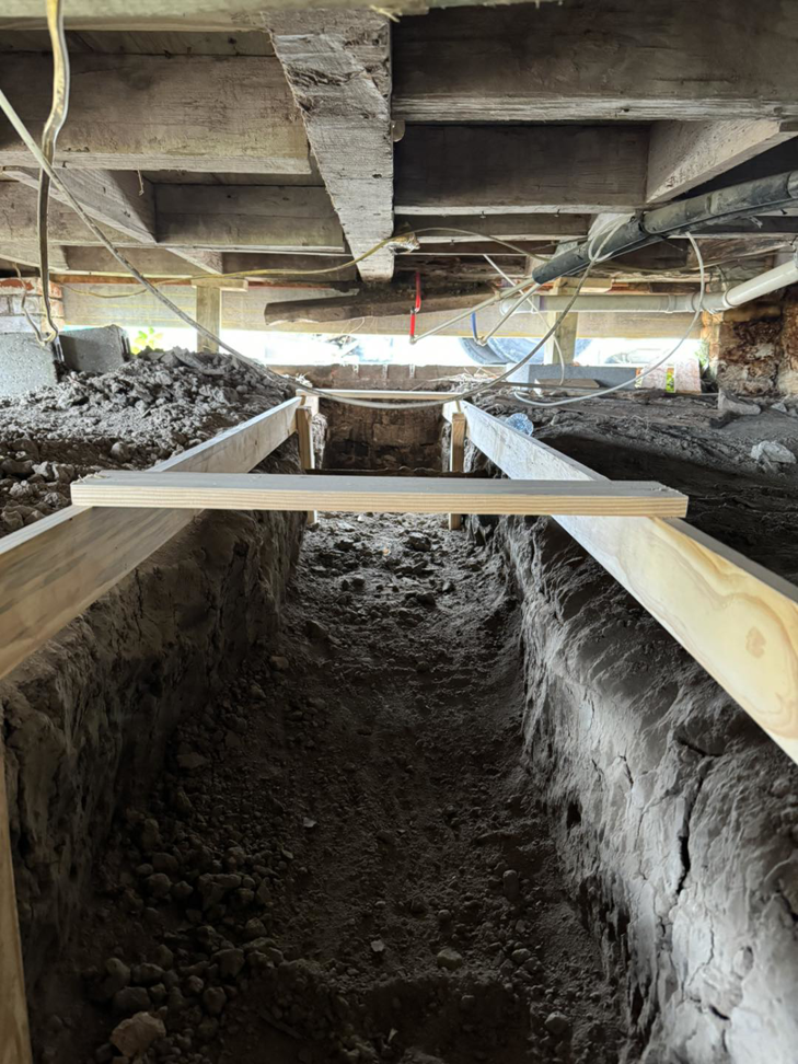 A trench dug in a crawl space under a house with wooden supports, showing handyman work by LA Pro Land Services llc in Houma, LA