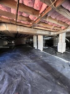 A crawl space with a black vapor barrier installed by Drip Dry Drainage in Cramerton, NC.